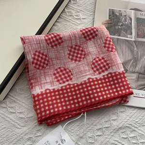 Close-up of red and white plaid pattern soft fabric scarf with tags on white texture