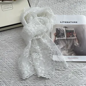 Close-up of white lace scarf with floral embroidery and pearl details on a desk
