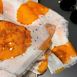 Detail of beige cotton scarf featuring orange watercolor prints and gold foil accents