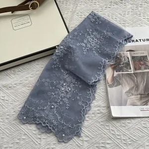 Detail of lace scarf with floral embroidery and hand-sewn pearls on light blue mesh fabric