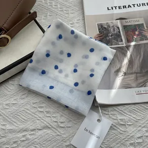 Elegant white polka dot silk scarf with gift tag on a magazine and leather bag