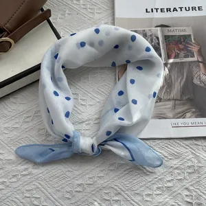 Soft white silk scarf with blue polka dots tied in a knot on a stylish lifestyle background