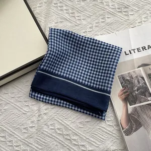 Detail van blauwe geruite katoenen sjaal met donkerblauwe rand op witte gebreide stof