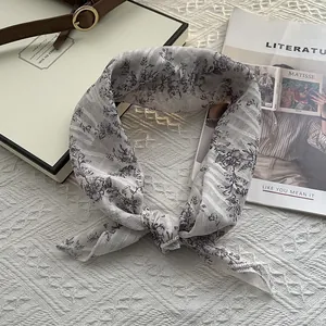 Détail du foulard en mousseline avec motif floral noir sur tissu crème noué avec soin