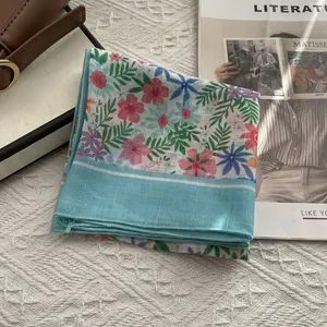 Détail d'un foulard en coton et lin à fleurs avec bordure bleue et motifs floraux