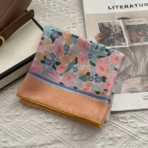 Floral cotton linen square scarf with orange border and gold rolled edges on a white cloth