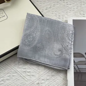 Close-up of light gray paisley cotton linen scarf with fine hem on a knitted background