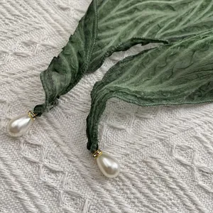 Detailopname van groene ruitvormige sjaal met parelhanger en goudkleurige accenten