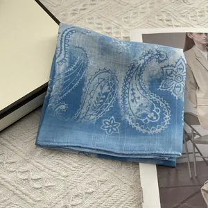 Detail of blue paisley pattern square scarf on soft knit background with gift box