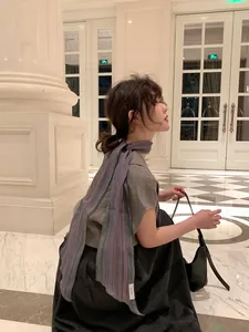Elegant woman wearing a striped linen scarf draped over a grey shirt in a classic hall