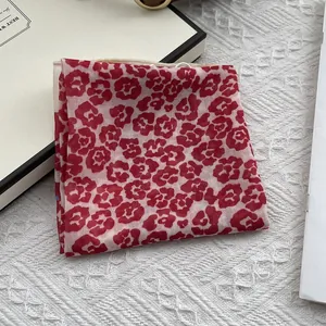 Macro detail of red floral print on sheer cream silk scarf with elegant hemmed edges