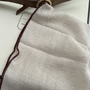 Detail of linen scarf fabric with burgundy stitched edges and premium leather strap accents