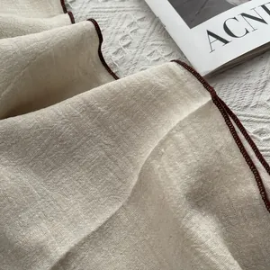 Detail of cream linen scarf with contrasting burgundy stitching on lace background