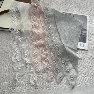 Detail showing lace embroidery and floral pom-pom trim on pastel cotton triangle scarves
