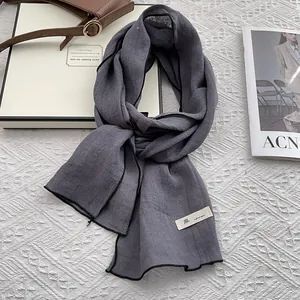 Detail of dark grey linen scarf with black trim and stitched label on a flat lay set