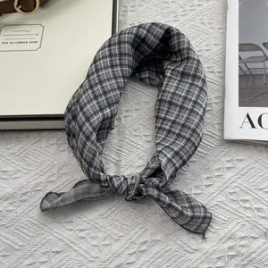 Dettaglio macro di un foulard di seta a quadri grigio-blu annodato su uno sfondo bianco