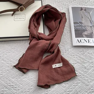 Macro detail of terracotta linen scarf with green contrast edge and woven brand label