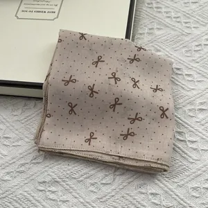 Detail of pink cotton linen scarf featuring dark brown bow patterns and polka dots