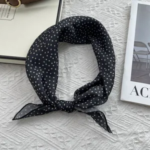 Detail of a vintage black square scarf with beige diamond pattern tied in a neat bow