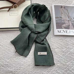 Detail of dark green linen scarf texture with brown stitched edge and nature fabric label