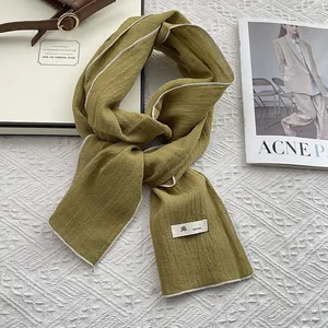Close-up of grass green linen scarf with white contrast stitching on a textured background