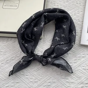 Black silk scarf with white bow and polka dot patterns next to a white gift box