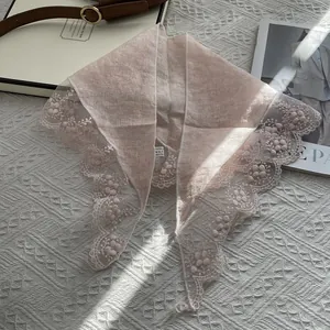 Detail of 100% linen scarf with floral lace trim and care label on a textured background