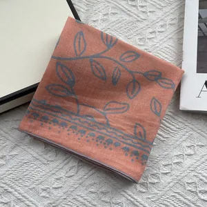 Close-up of brick red cotton linen scarf featuring blue leaf prints and wavy hem