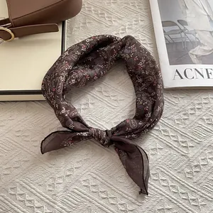 Detail of dark brown silk-feel paisley square scarf tied gracefully on a soft background