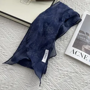 Deep blue linen skinny scarf with subtle floral print on a textured white surface