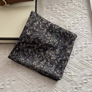 Detailed macro view of black paisley silk scarf texture on minimalist beige backdrop