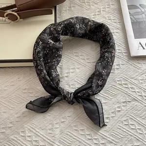 Detail of a black paisley silk scarf with knot design on woven white background