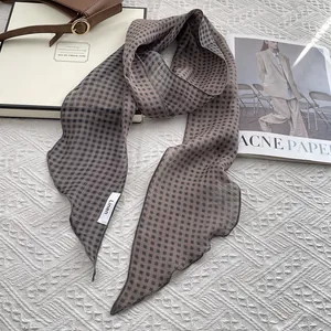 Detail shot of a brown plaid linen skinny scarf paired with a luxury leather handbag