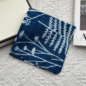Close-up of a dark blue cotton linen scarf with white floral leaf patterns folded neatly