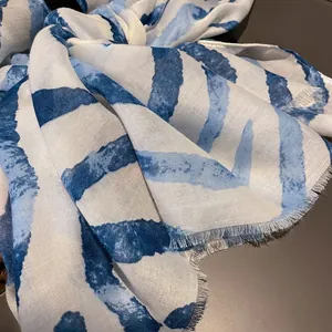 Detail of blue gradient striped scarf featuring frayed fringe and soft cotton fabric