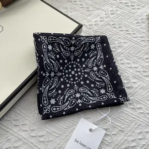 Macro detail of black paisley silk scarf with white pattern near a beige gift box