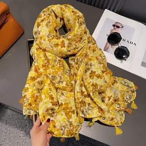 Detail of yellow floral scarf with tassels next to orange bag and sunglasses