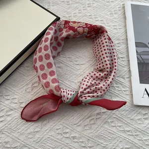 Détail d'un foulard carré à pois rouges et blancs noué sur un fond en maille blanche