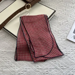Detail of red and white plaid linen scarf with fine dark blue stitched edges on a flat lay