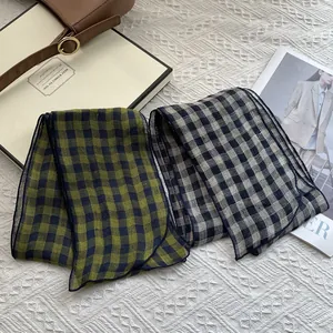 Close-up of lightweight checkered linen scarves in green and beige on white texture