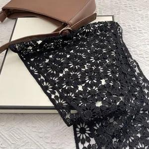 Close-up of black floral lace shawl with hollow daisy embroidery on a brown leather bag