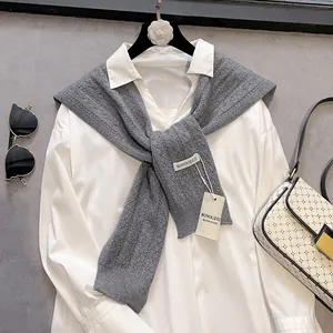 Detail of grey hollow-out knit shawl featuring handmade brand label on white shirt