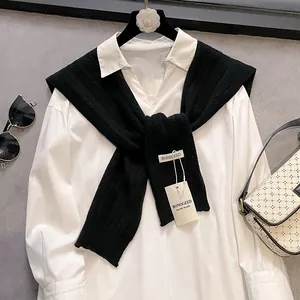 Detail of a white cotton shirt layered with a black knit shawl and fashion accessories