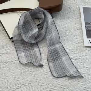 Gray and white plaid thin linen scarf on quilted mat with magazine and brown leather bag