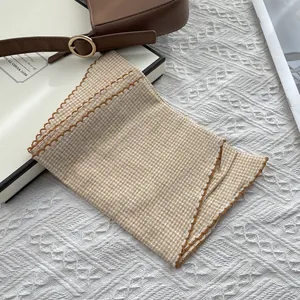Close-up of khaki plaid cotton scarf featuring delicate brown embroidered wavy edges