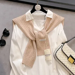 Detailed view of beige hollow-out knit shawl texture and woven brand label on white shirt