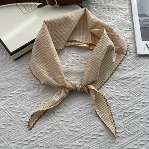 Detailed view of plaid cotton scarf with decorative scalloped edges on textured background