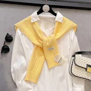 Detail of bright yellow knit shawl with hollow texture and handmade tag over white shirt