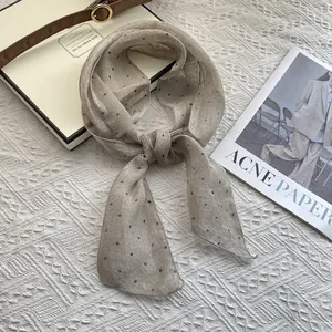 Detail of light beige polka dot linen scarf displayed with minimalist fashion accessories