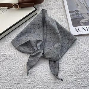 Detail of grey diamond-patterned cotton linen scarf tied on a white textured background